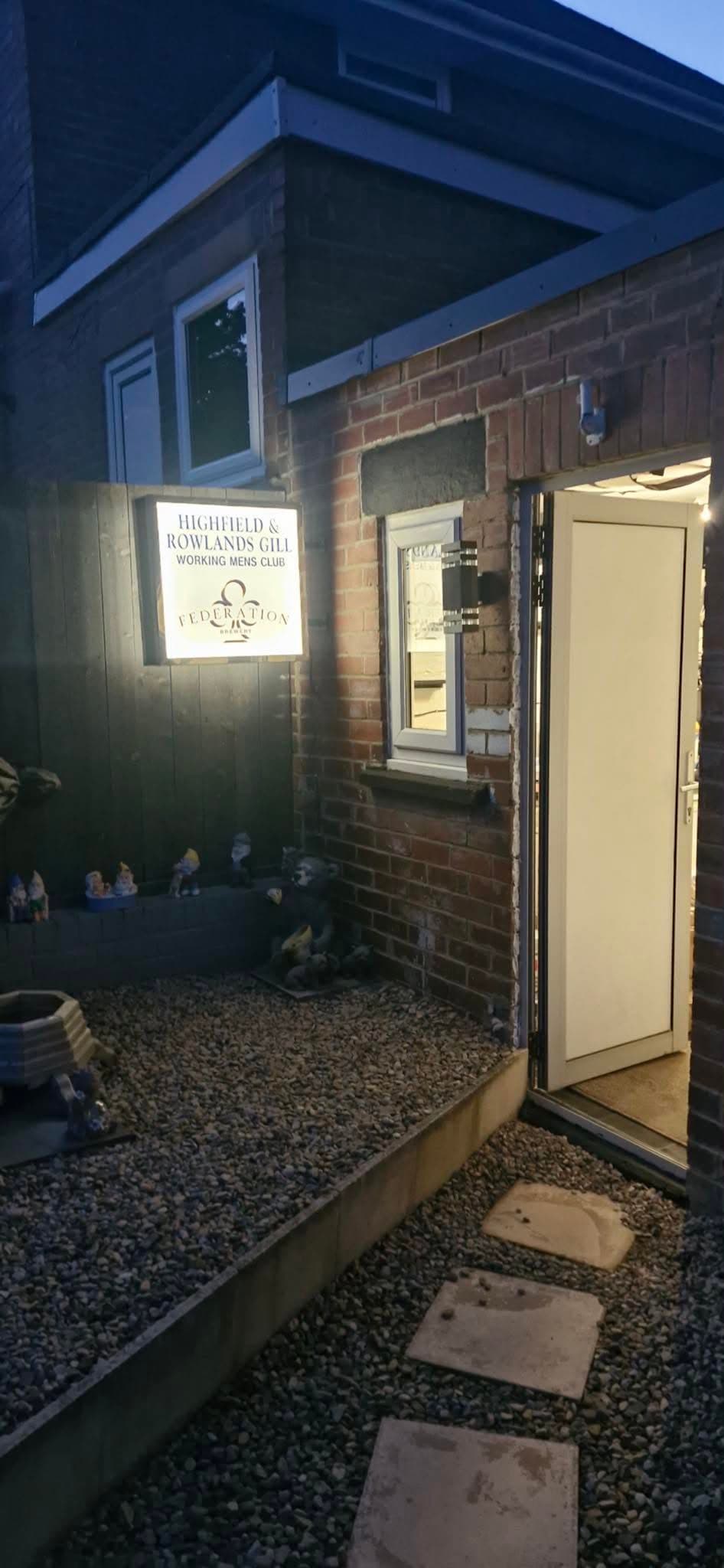 Illuminated wall-mounted sign lighting at a working men's club entrance