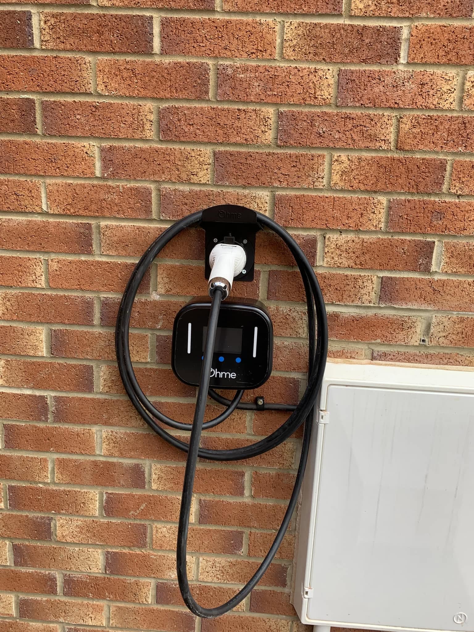 Ohme home EV charger wall-mounted on brickwork with a neatly coiled cable