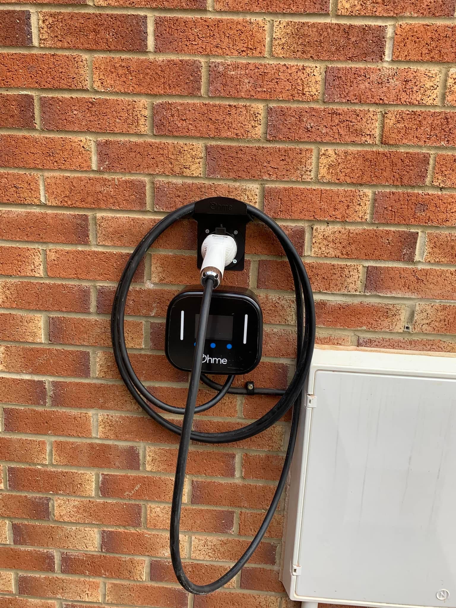 Ohme home EV charger wall-mounted on brickwork with a neatly coiled cable
