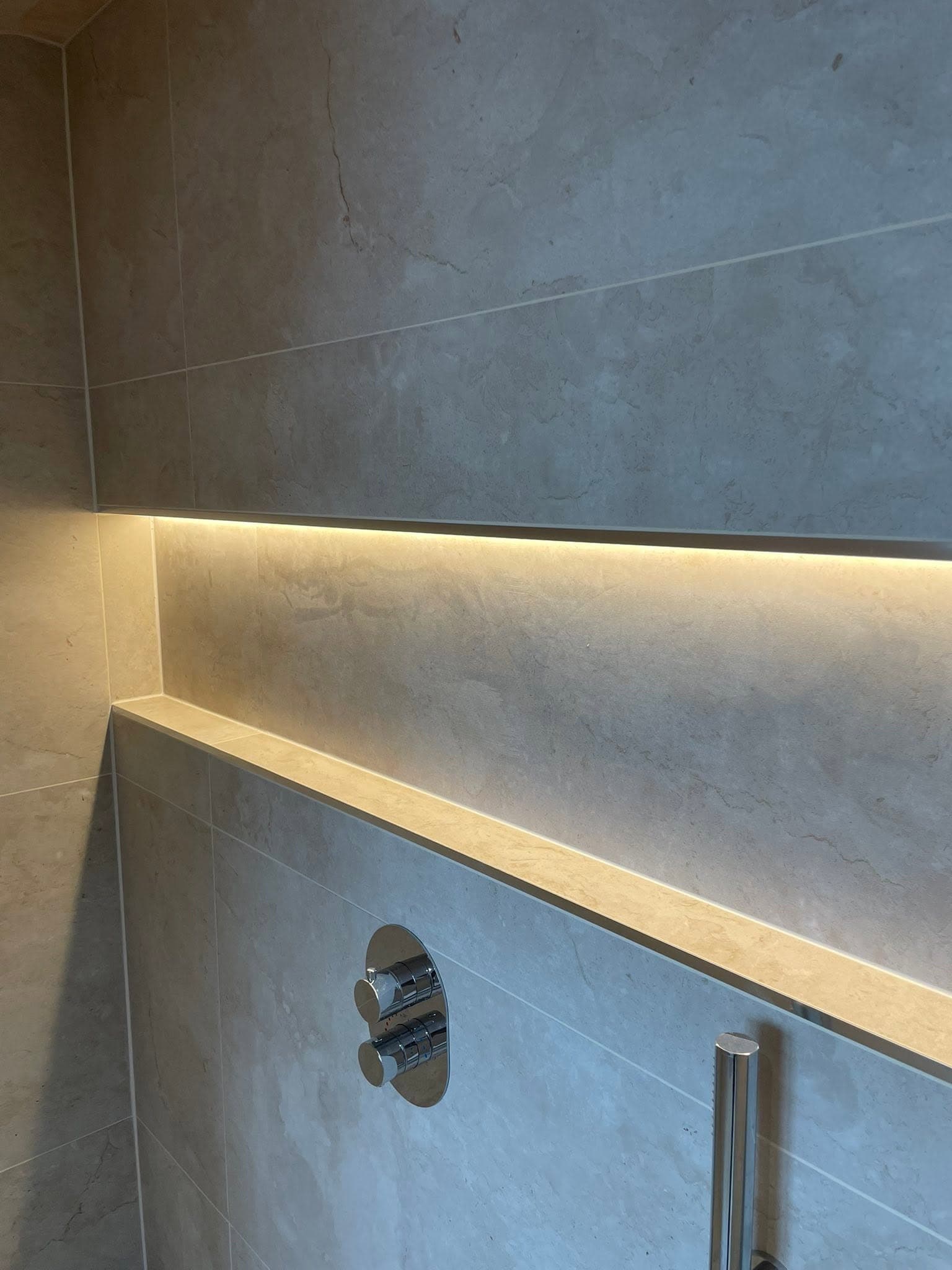 Walk-in shower with stone-effect tiles and warm LED strip lighting recessed into a wall shelf niche
