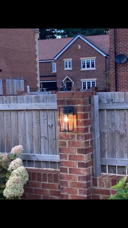 Brick garden pillar fitted with a glass box lantern glowing warm at dusk