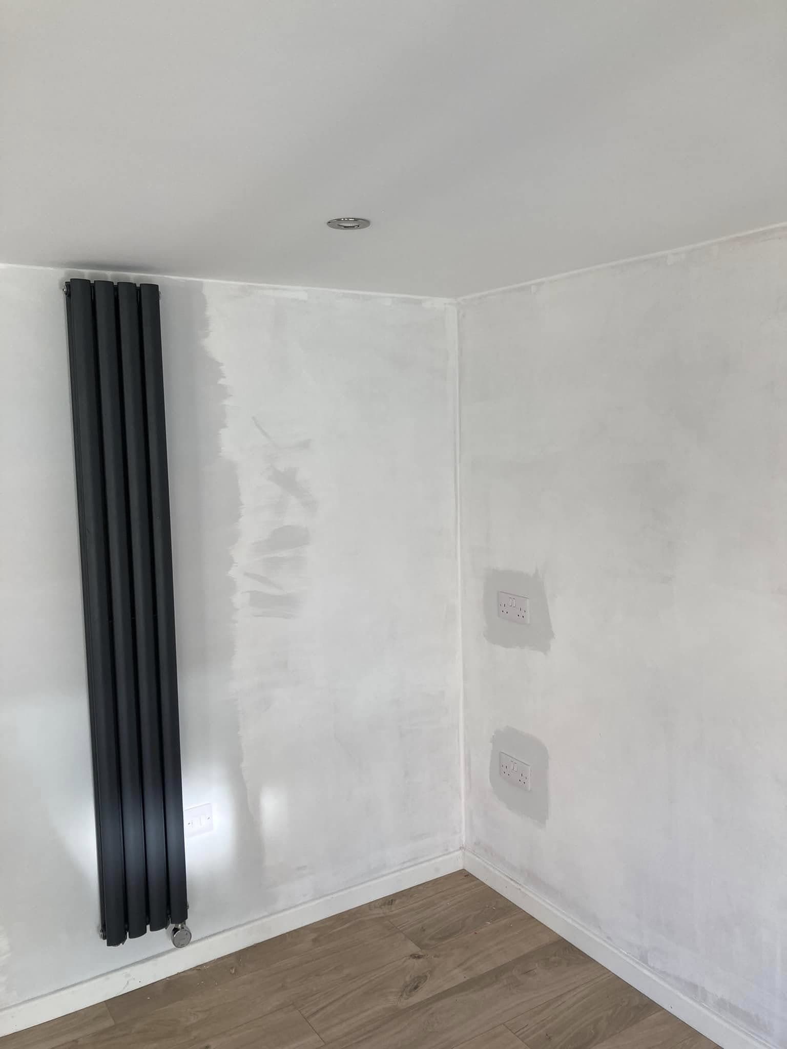 Newly finished room with a panel radiator, double sockets and a recessed ceiling downlight