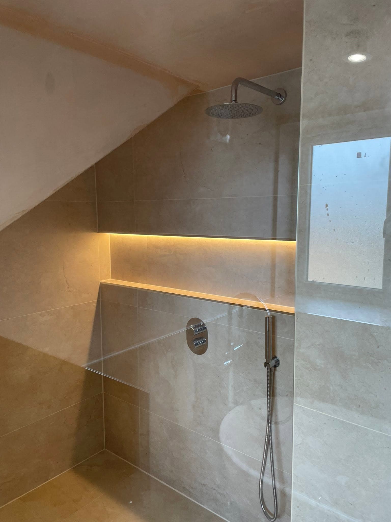 Loft shower under a sloped ceiling with a rainfall head and warm LED-lit niche