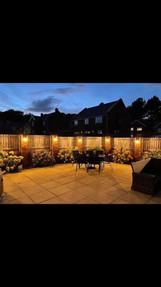 Garden patio at dusk lit with fence-mounted lanterns across the flower borders