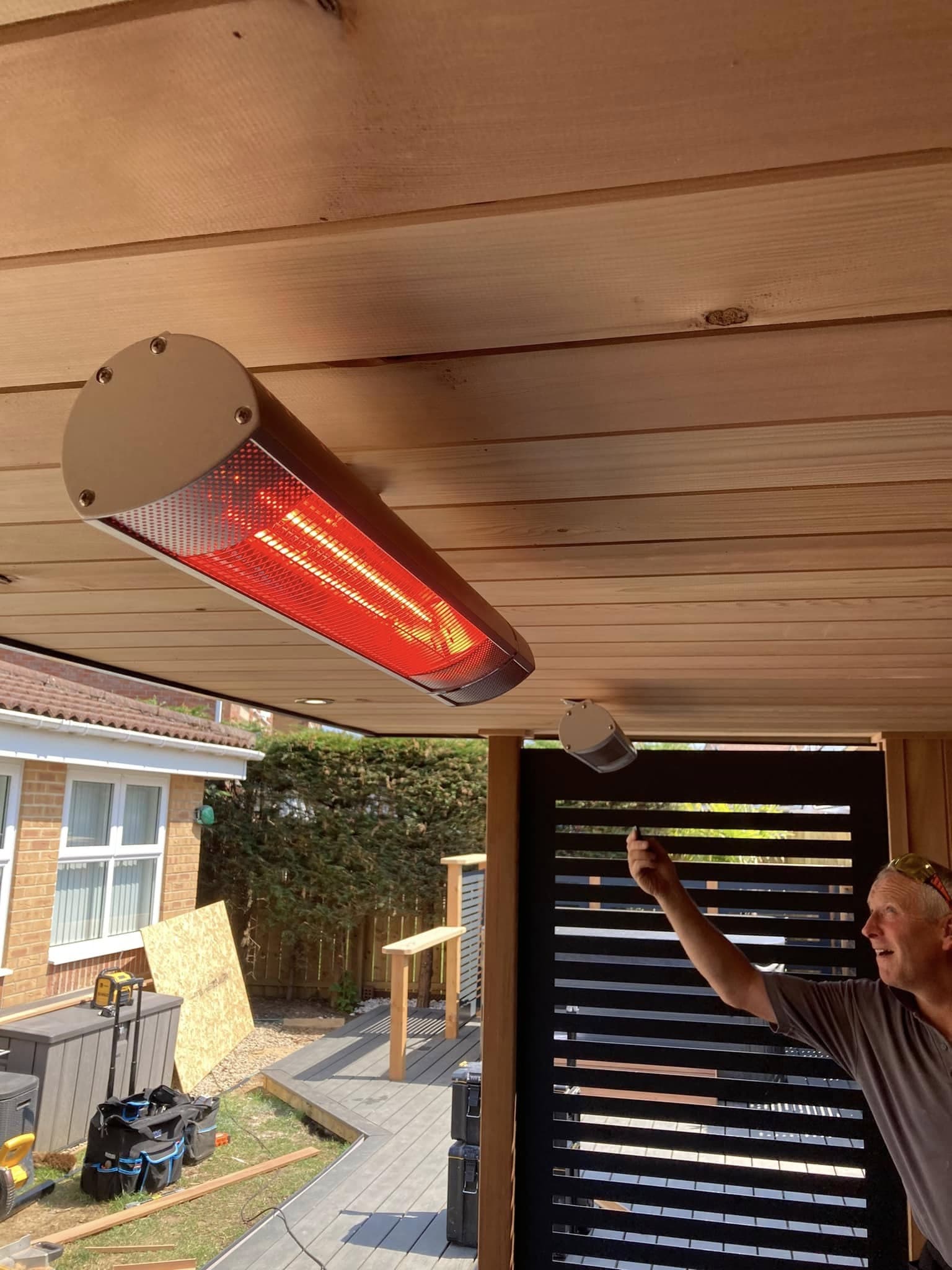 Wall-mounted infrared patio heater glowing beneath a cedar-clad garden canopy
